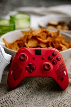 Close-up of a red gaming controller near bowls of snacks, ideal for gaming lifestyle themes.