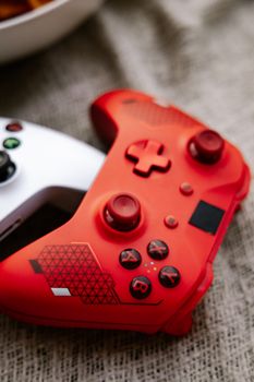 Vivid close-up of red and white Xbox wireless game controllers on textured surface.