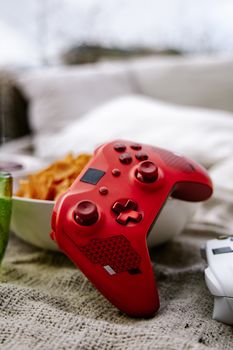 Close-up of a red Xbox wireless controller on a textured surface with a bowl of chips nearby.