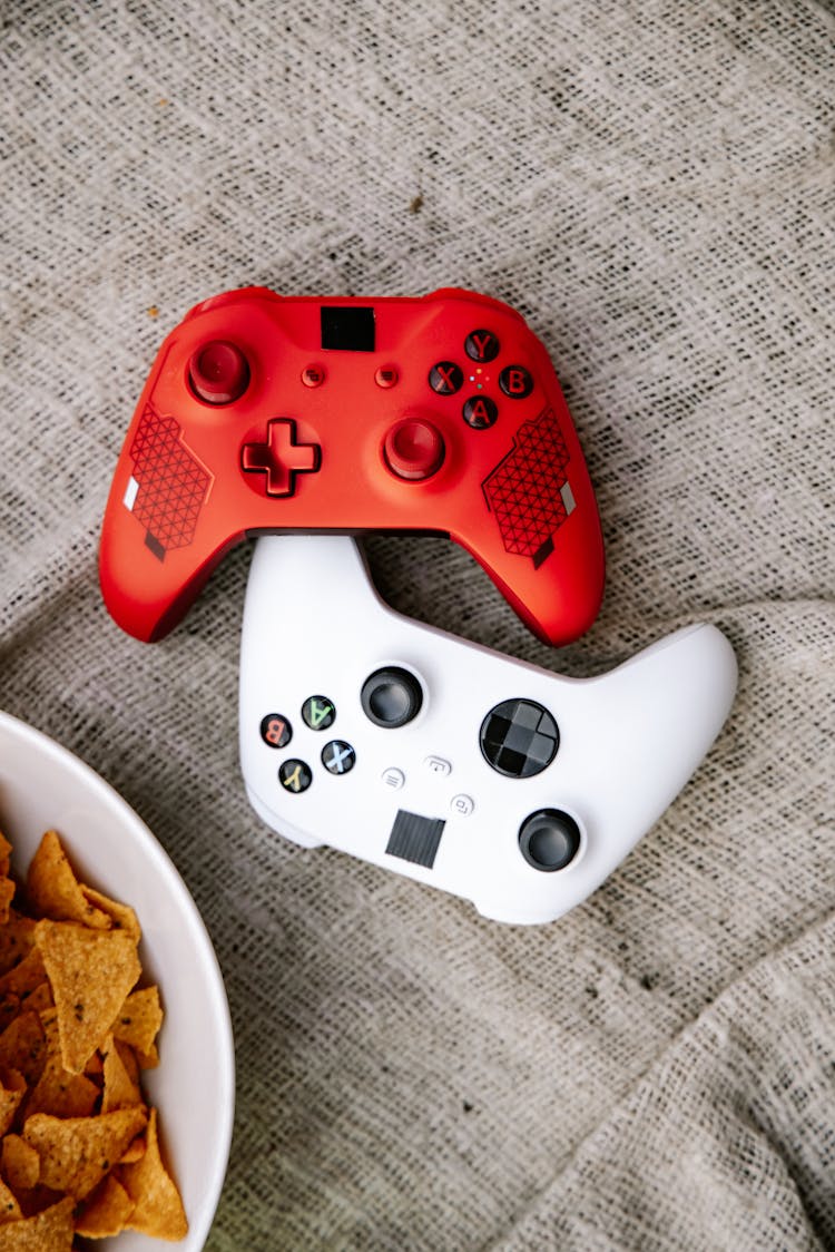 White And Red Game Controllers Beside A Bowl Of Chips