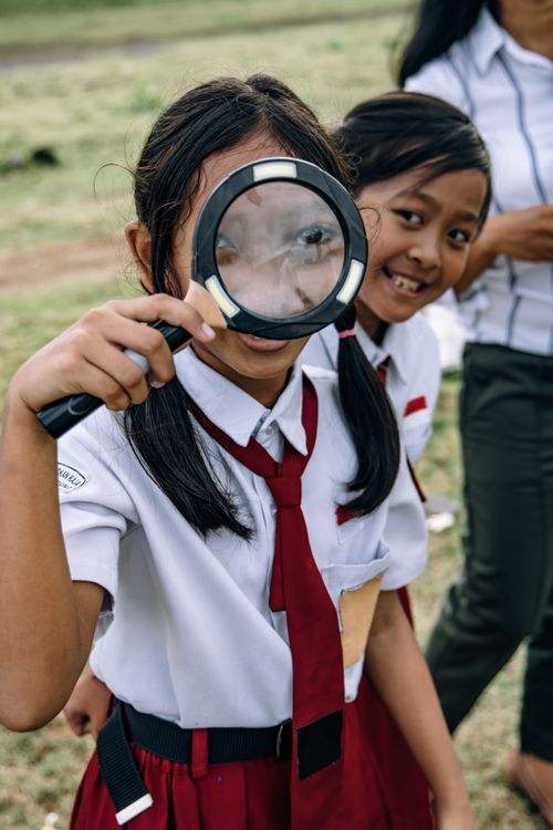 Free Joyful girls in school uniforms having fun with a magnifying glass outdoors. Stock Photo