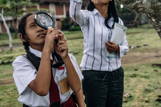 Students in school uniforms using a magnifying glass for outdoor exploration. Educational outdoor activity.
