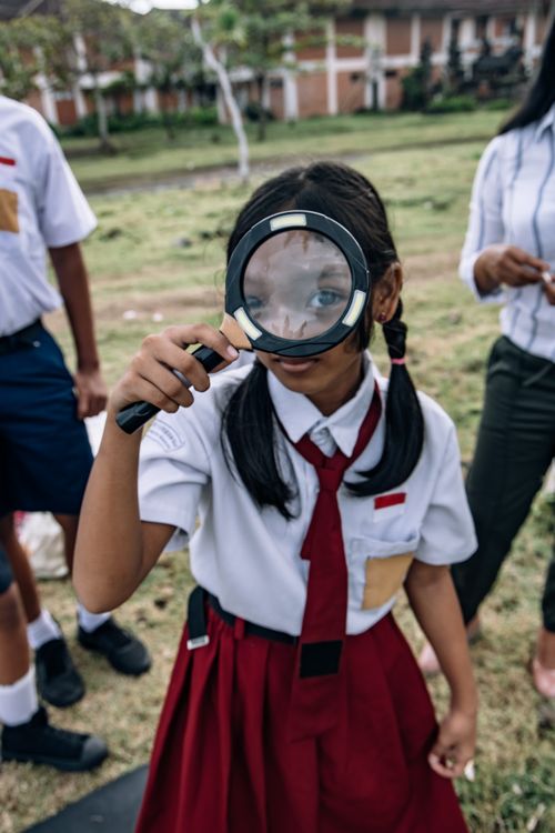 Free Young girl in school uniform using a magnifying glass outdoors, curious exploration. Stock Photo