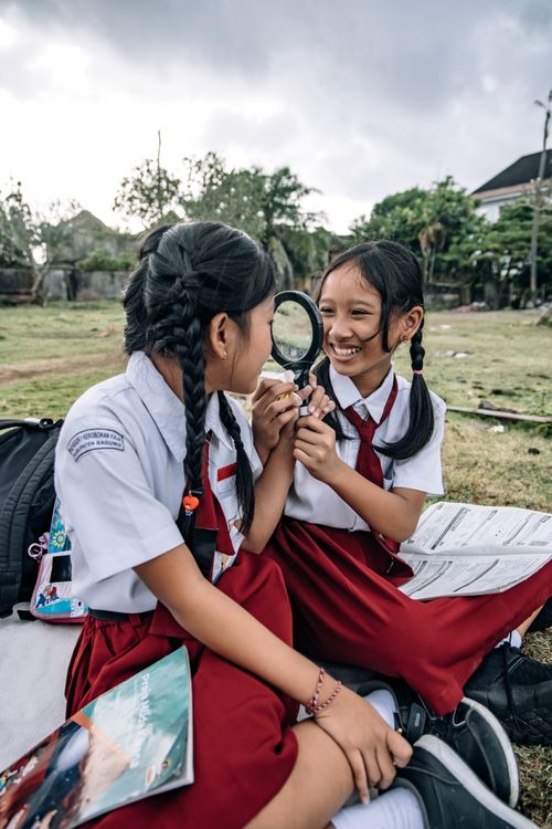 Free Two schoolgirls in uniforms using a magnifying glass outdoors, symbolizing curiosity. Stock Photo