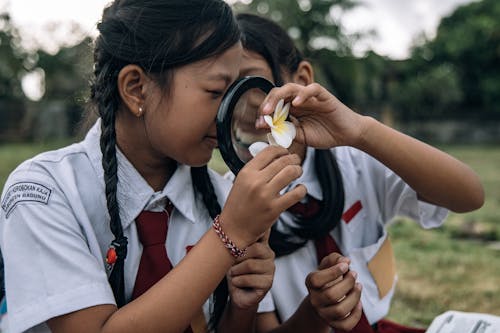 Two Girls in School Uniforms Using a Magnifying Glass