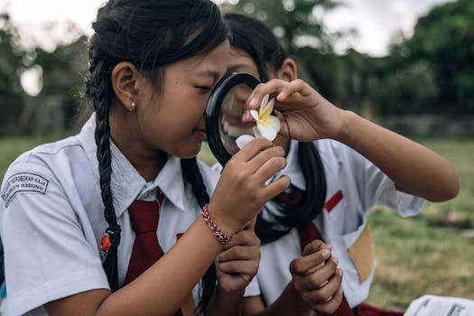 Children in school uniforms examining a flower with a magnifying glass outdoors.