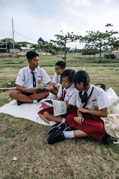 A Group of Students Reading Books while Sitting on a Grassy Field