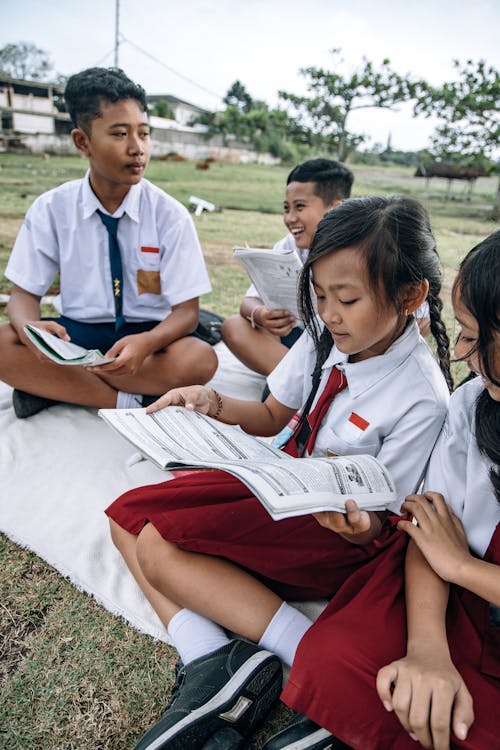 Students in School Uniforms Studying while Sitting on Picnic Blanket
