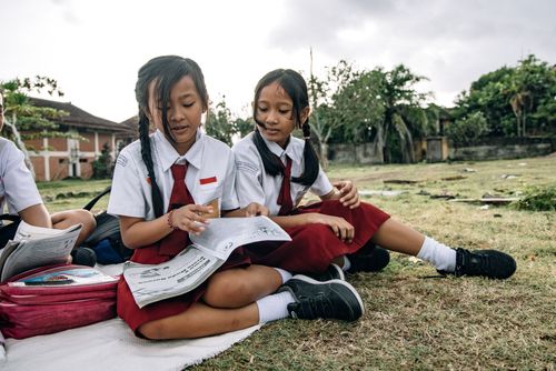 Free Two schoolgirls in uniforms reading together outdoors on a sunny day. Stock Photo