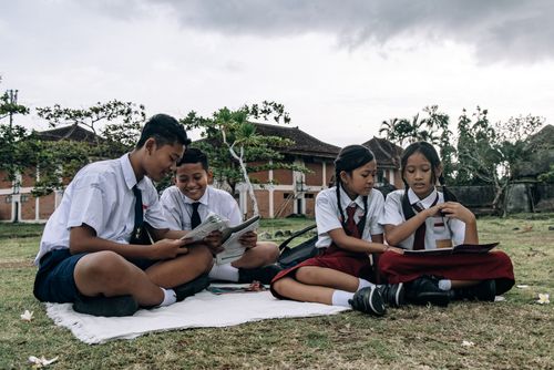 Free Group of children studying together outdoors in school uniforms on a picnic blanket. Stock Photo