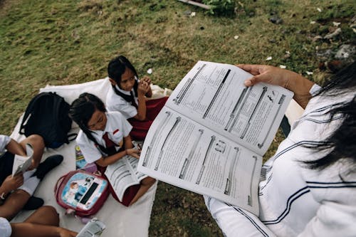 Female Students Sitting on the Field while Reading Books