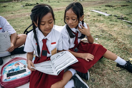 Two young students in school uniforms reading outdoors on a sunny day.