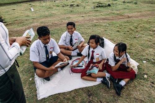 Free Group of students in uniforms reading together on a grassy field. Stock Photo