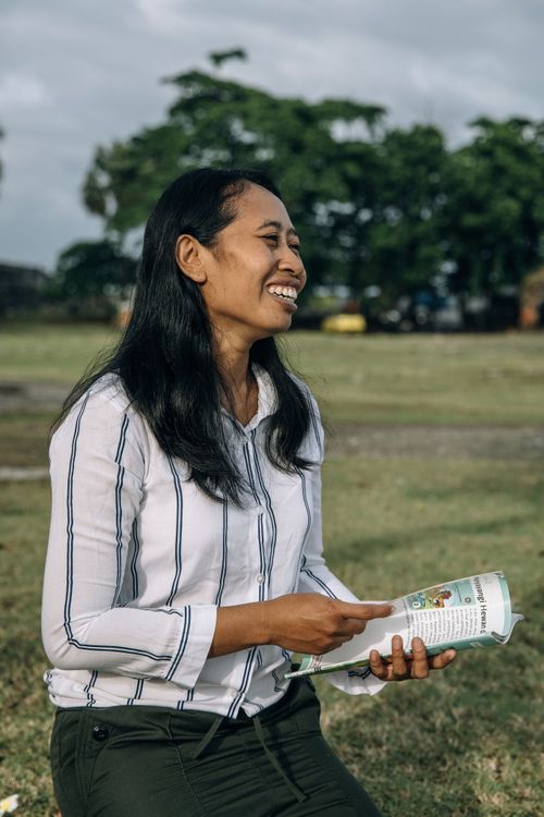 Free Asian woman enjoying a book while sitting outdoors in a sunny park. Stock Photo