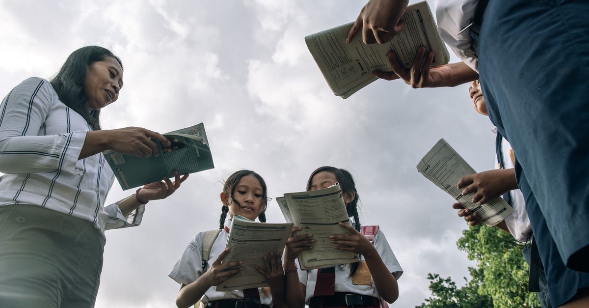 Students and teacher in school uniforms reading books outdoors under a cloudy sky.