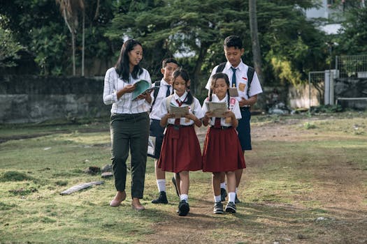 Students in uniforms walking with a teacher outdoors, holding books and papers.