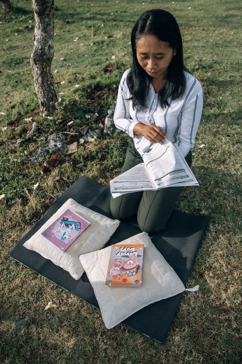 Free Asian woman reading a book outside on a sunny day, enjoying nature. Stock Photo