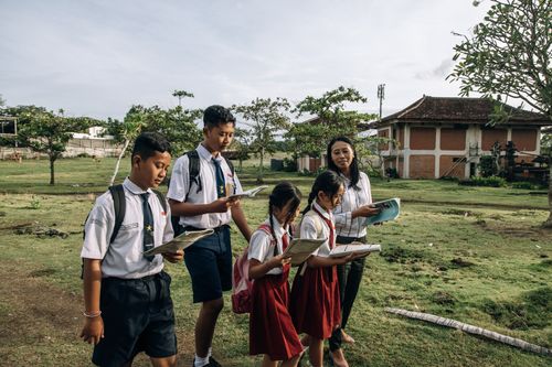 Free Group of students in school uniforms reading outdoors with their teacher on a sunny day. Stock Photo