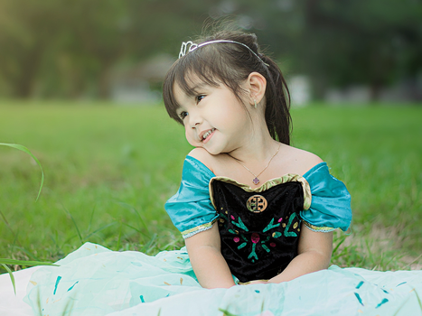 Adorable young girl in princess gown smiling outdoors on grass.