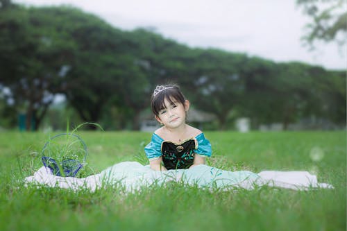 Girl Wearing a Princess Costume Sitting on Green Grass Field