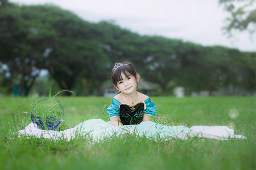Adorable girl in a princess outfit sitting on grass, smiling warmly.
