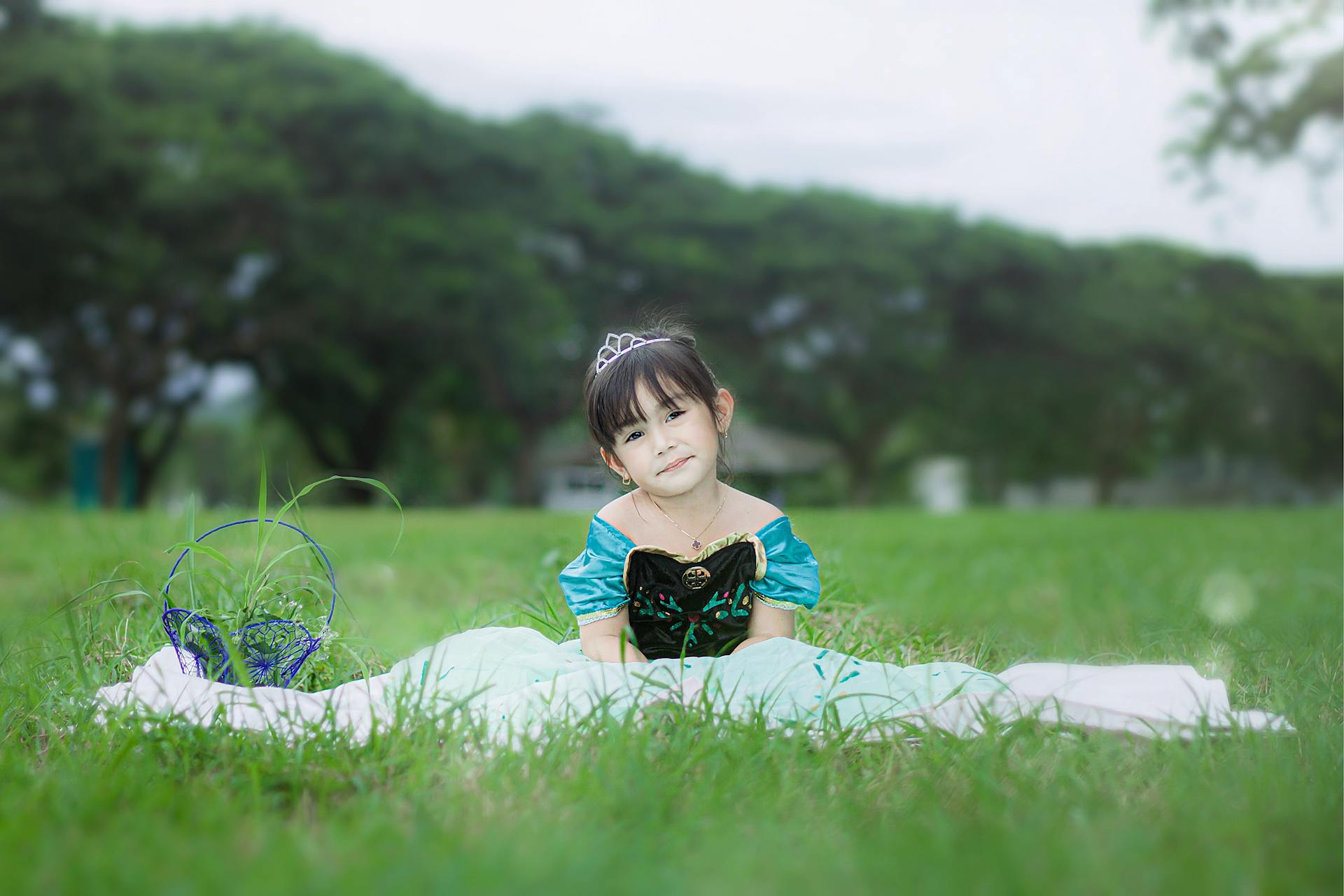 Adorable girl in a princess outfit sitting on grass, smiling warmly.