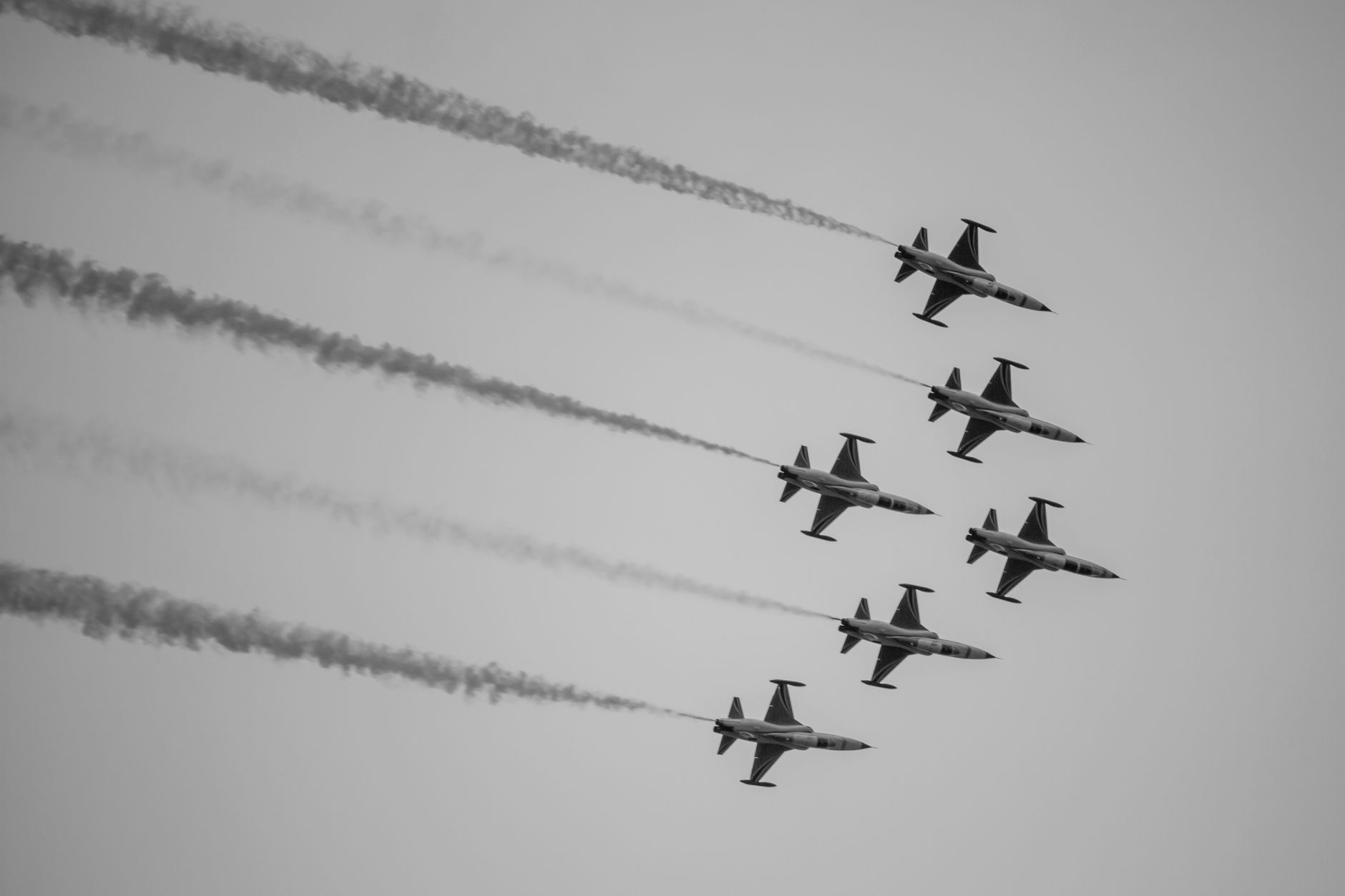 A black and white image of military jet aircrafts in formation flight with smoke trails in the sky.
