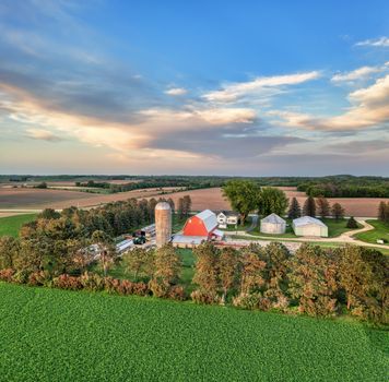 Aerial shot of a picturesque farm in Minnesota with vibrant fields and rustic buildings under a blue sky.