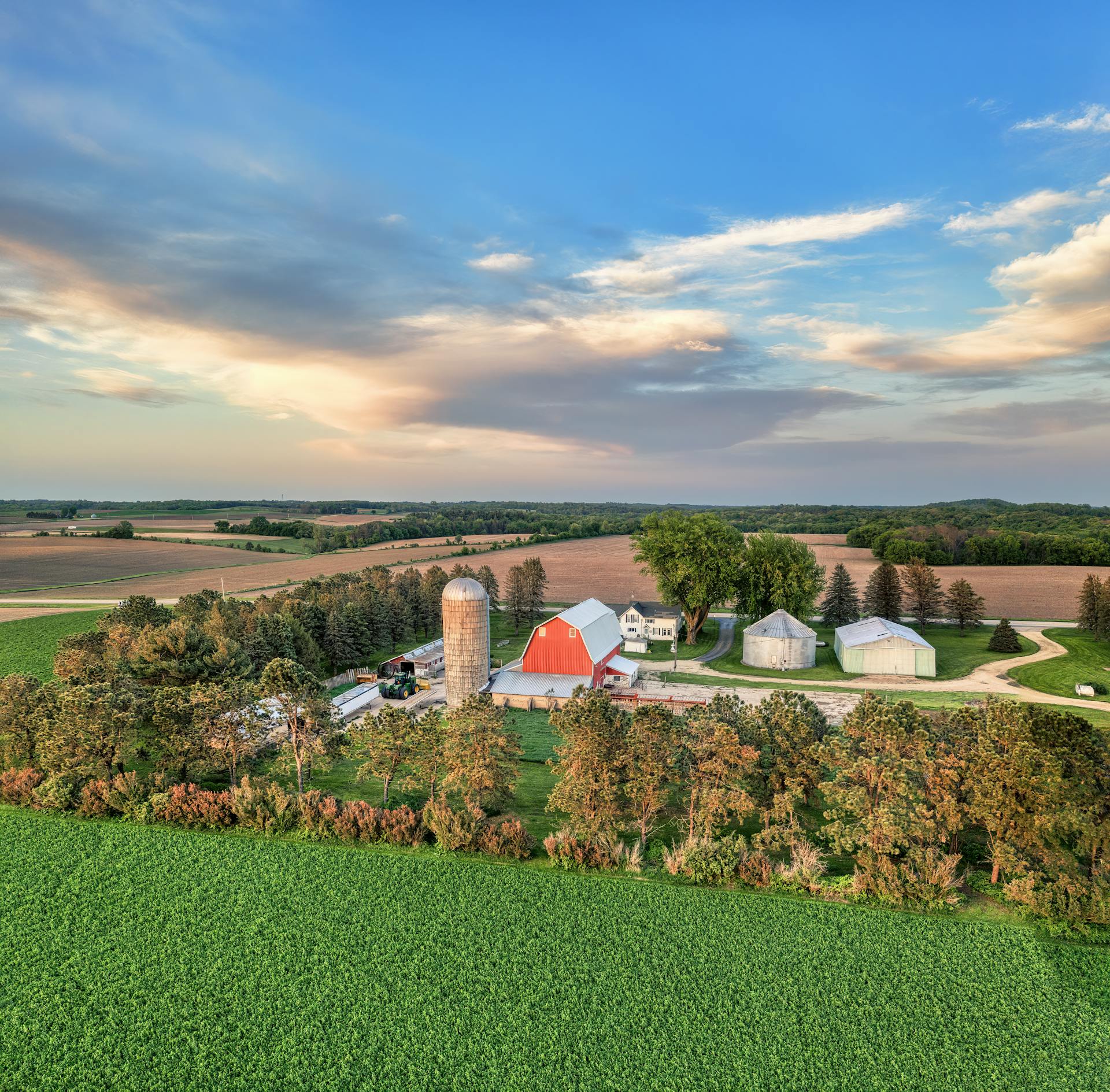 Aerial shot of a picturesque farm in Minnesota with vibrant fields and rustic buildings under a blue sky.