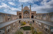 Scenic view of the Agha Bozorg Mosque's historic courtyard in Kashan, Iran under a partly cloudy sky.