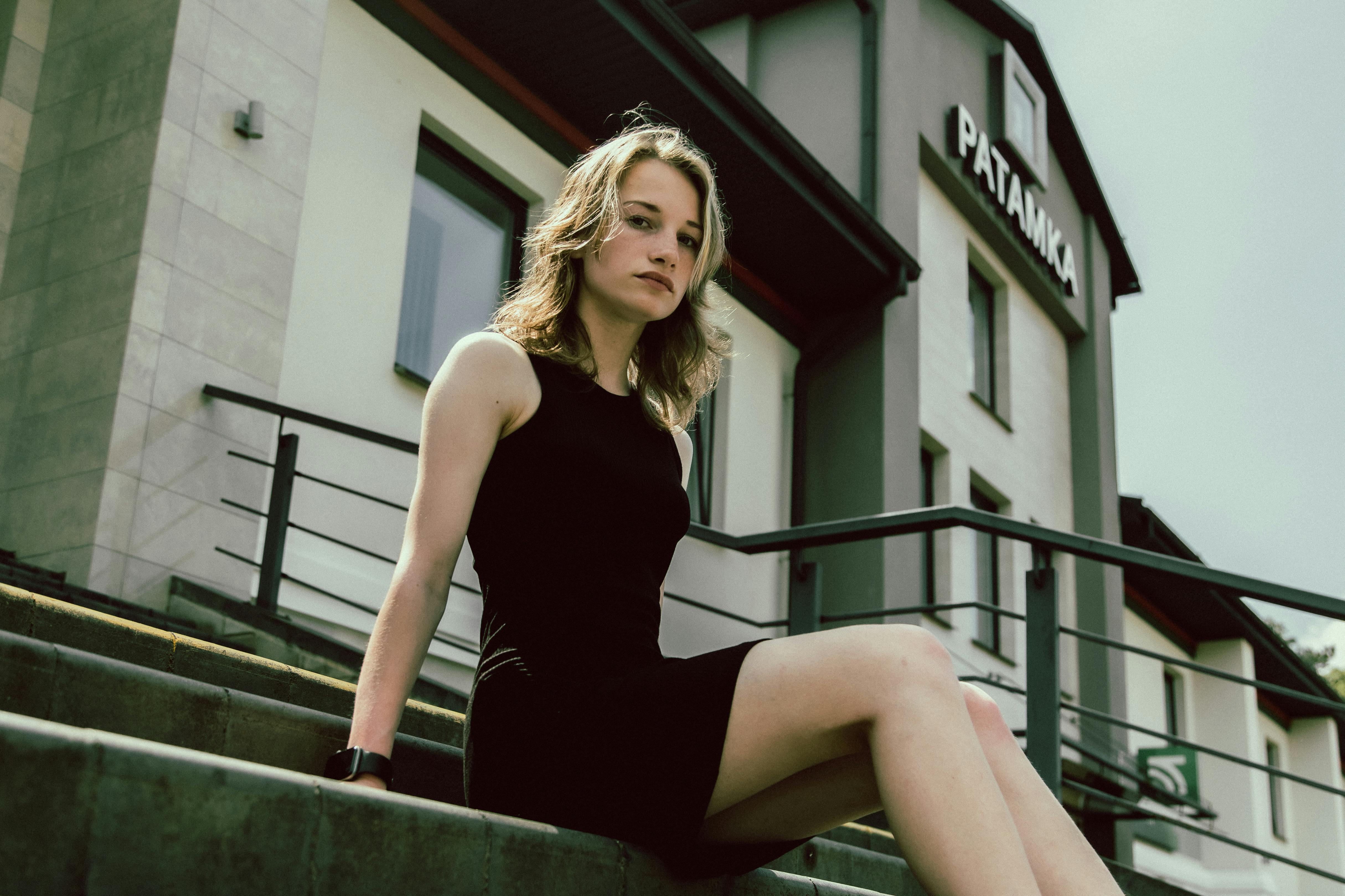 Portrait of a woman in a black dress sitting on stairs outside a building.