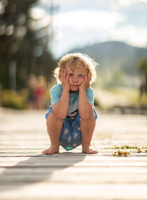 Free A child sitting outdoors on a sunny day, looking thoughtful and slightly sad. Stock Photo