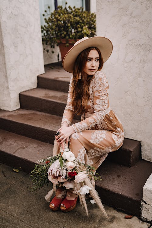 Woman in a Brown Embroidered Floral Dress Sitting on the Steps with a Bouquet in Her Hand