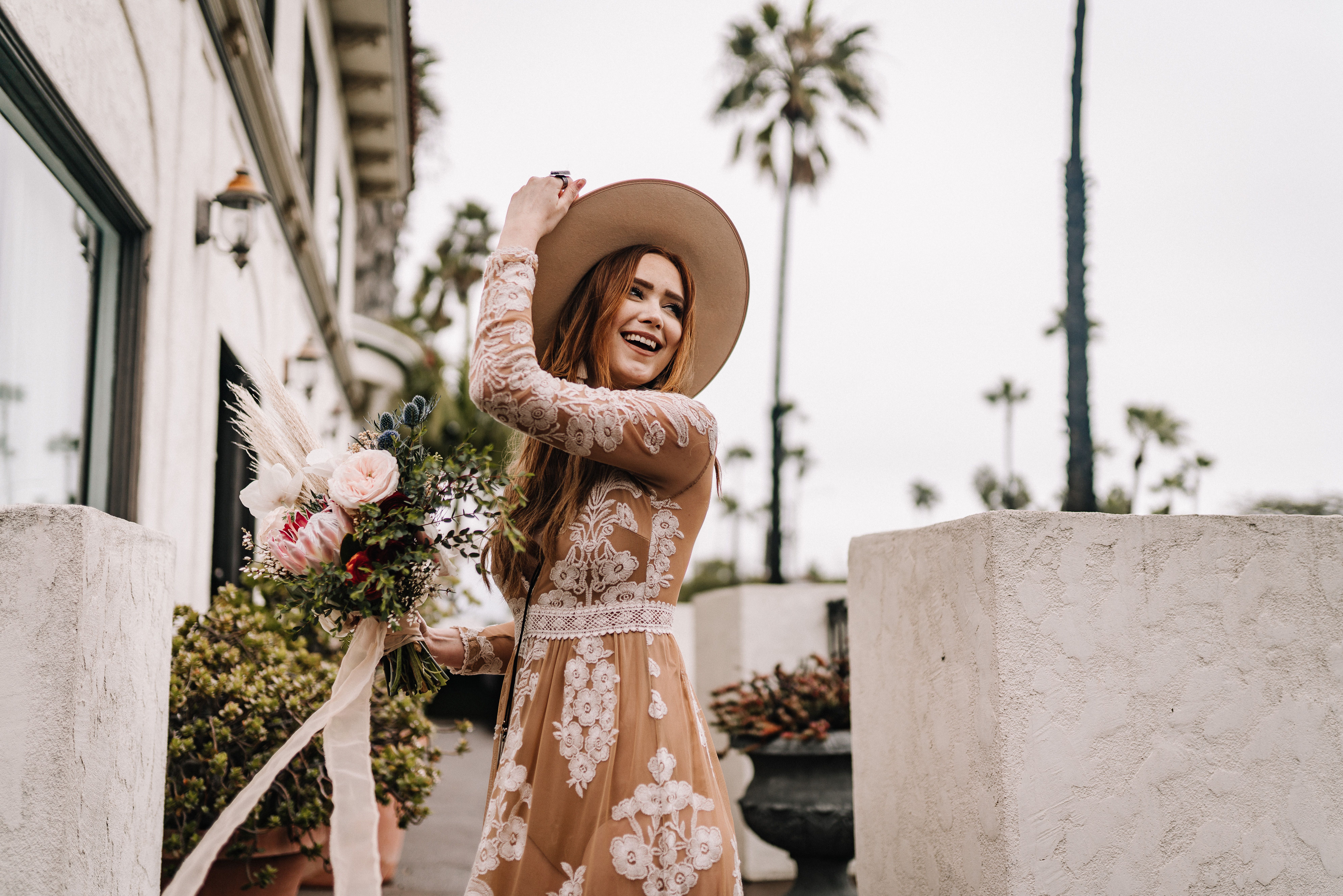 A smiling bride in a boho chic dress holding a bouquet, celebrating outdoors on a pleasant day.