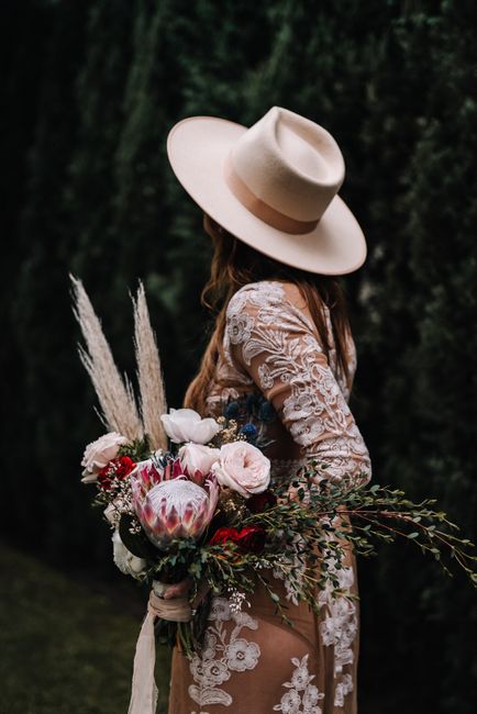 Boho chic woman in a brown dress and beige hat, holding a vibrant floral bouquet outdoors.