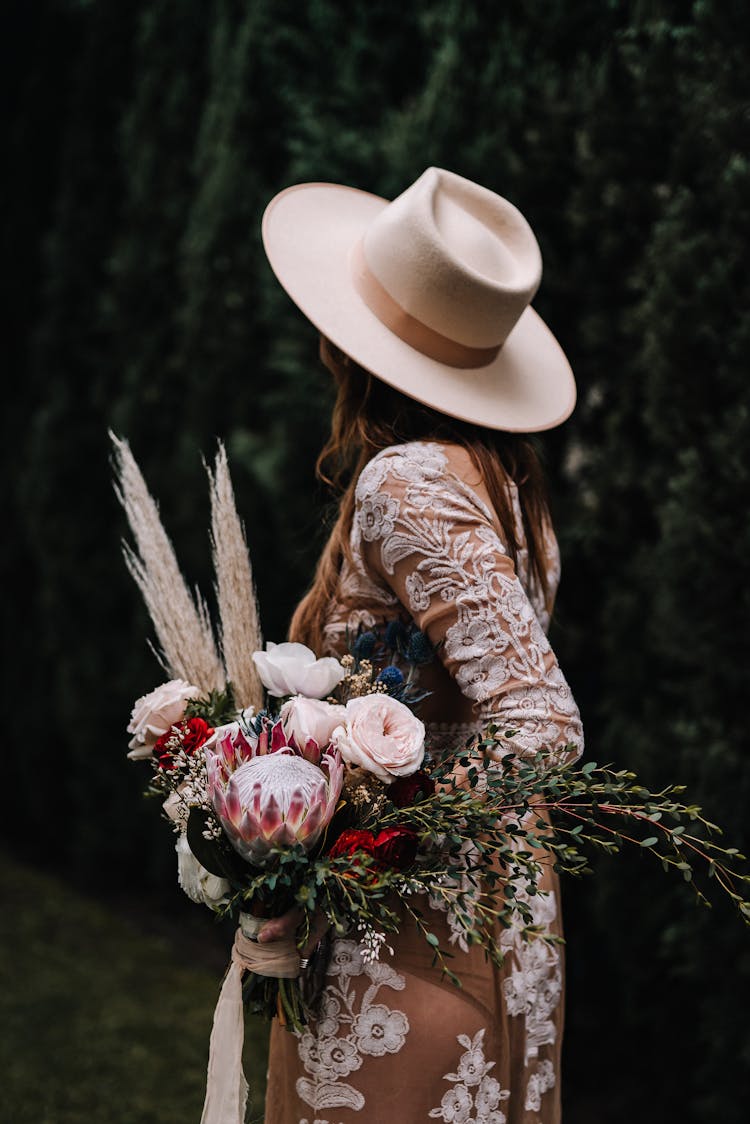 Woman In A Brown Embroidered Floral Dress And A Beige Hat Carrying A Bouquet Of Flowers