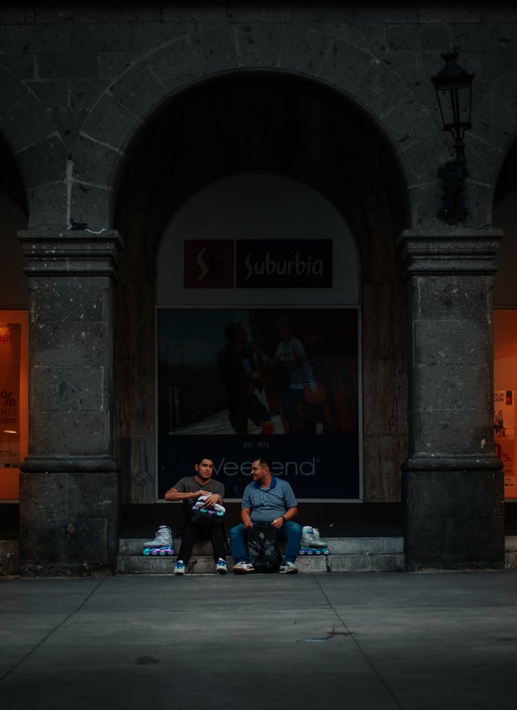 Men Sitting On A Curb In City With Roller Skates 