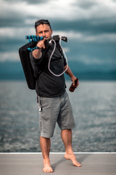 A man with a backpack pointing towards the camera while enjoying a beachside leisure time with a drink.