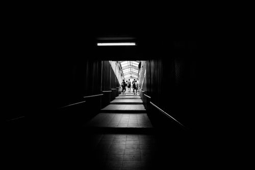 Free A dark, monochrome image of people walking through an underground passageway. Stock Photo
