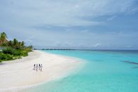 A group of people walking along a pristine tropical beach under clear blue skies.
