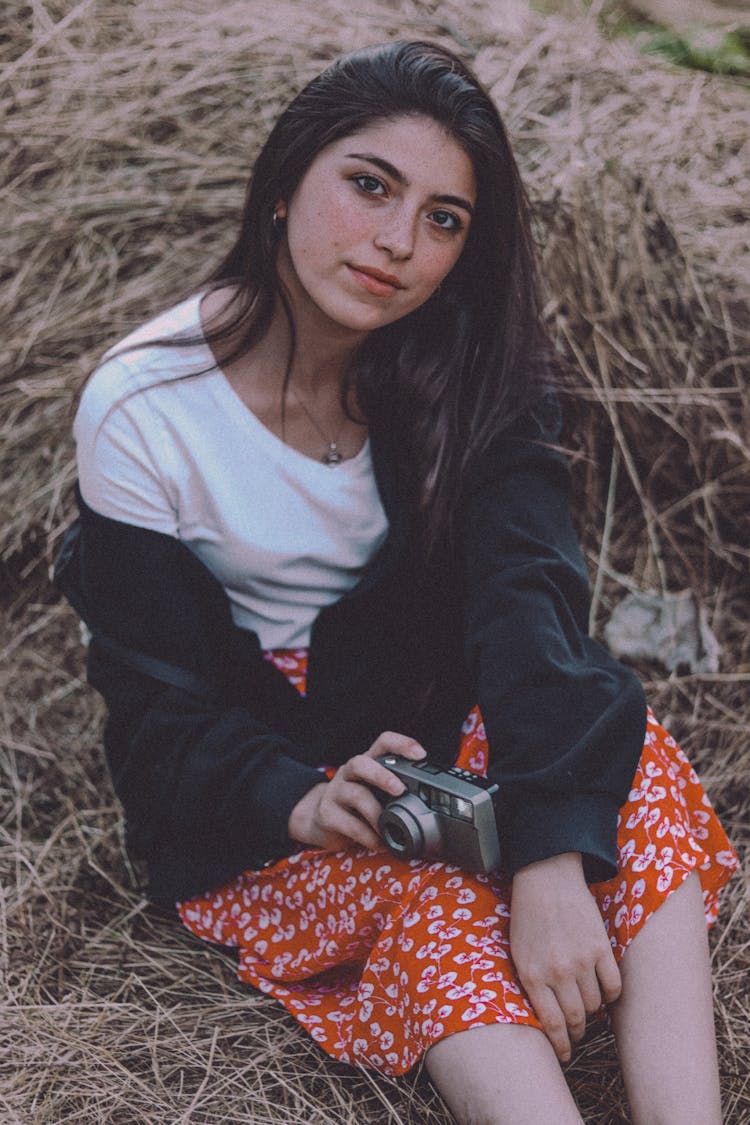 A Woman Holding A Camera While Sitting On Hay