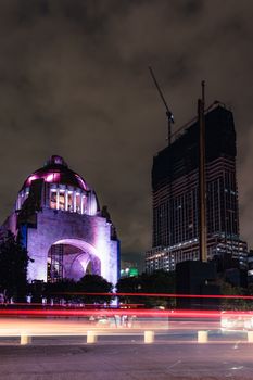 Long exposure of an illuminated monument and skyscraper at night with traffic light trails.