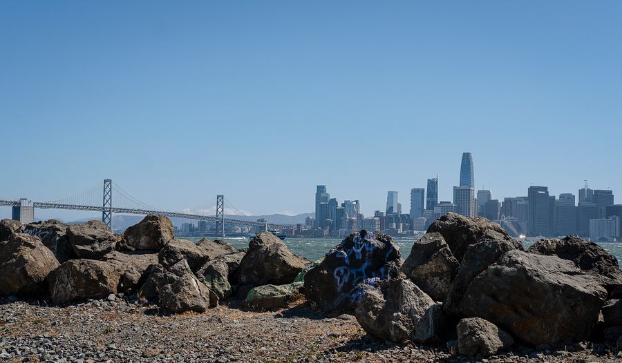The San Francisco skyline and the Bay Bridge seen across the water from a rocky shoreline