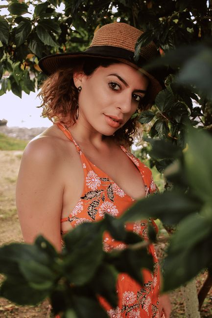Portrait of a woman in a floral dress and hat, surrounded by lush greenery, exuding elegance and beauty.