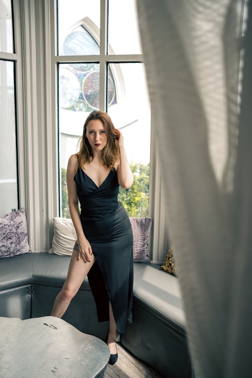 A Woman in a Black Dress Standing beside a Window