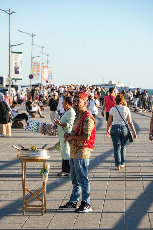 Free A vibrant street with a vendor selling goods surrounded by a crowd on a sunny day. Stock Photo