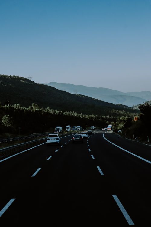 Free A serene highway view with cars driving through picturesque mountain scenery at dusk. Stock Photo
