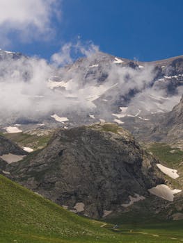 A striking mountain scene with fog, snow patches, and rugged terrain under a clear blue sky.