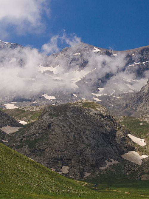 Free A striking mountain scene with fog, snow patches, and rugged terrain under a clear blue sky. Stock Photo