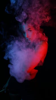 Mysterious woman enveloped in colorful red and purple smoke in a dimly lit environment.